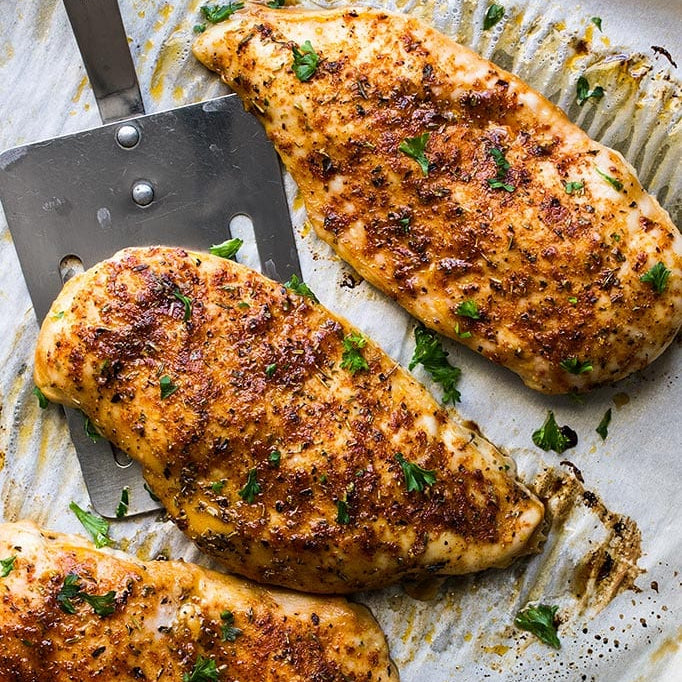 Baked chicken breasts on a baking sheet with a spatula
