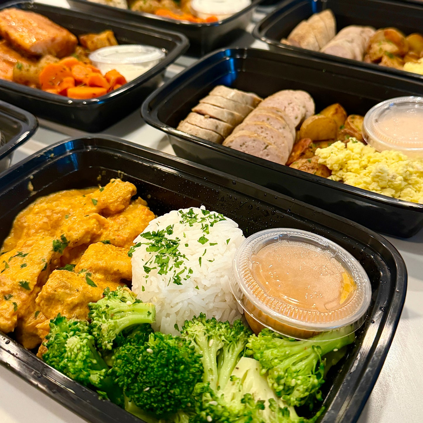 close-up of gourmet meal prep containers with organic proteins, rice, vegetables, and house-made sauces, ready for pickup or delivery