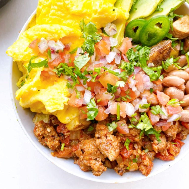 Plate of scrambled eggs with salsa, beans, and avocado on a white plate.