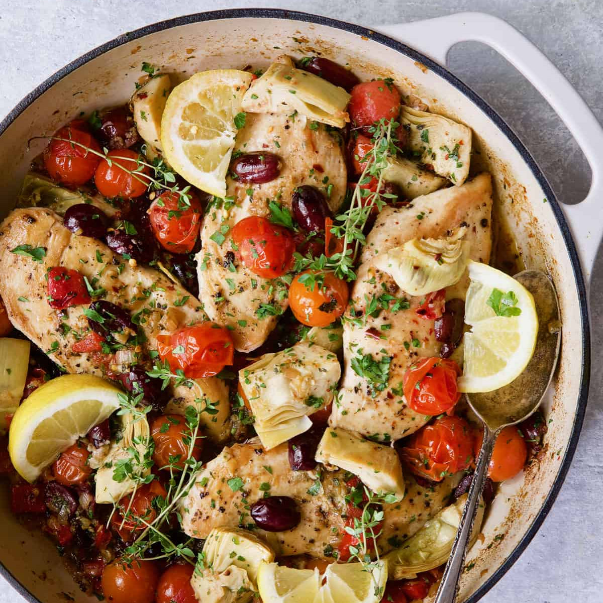 Dish of chicken with lemon, tomatoes, and olives in a white pan on a light background