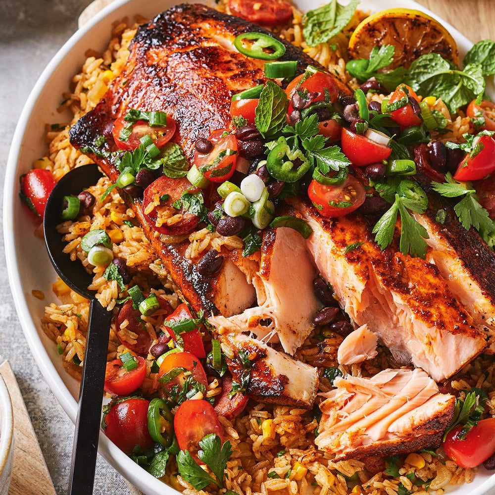 Salmon dish with rice, vegetables, and a spoon in a white bowl on a wooden surface.