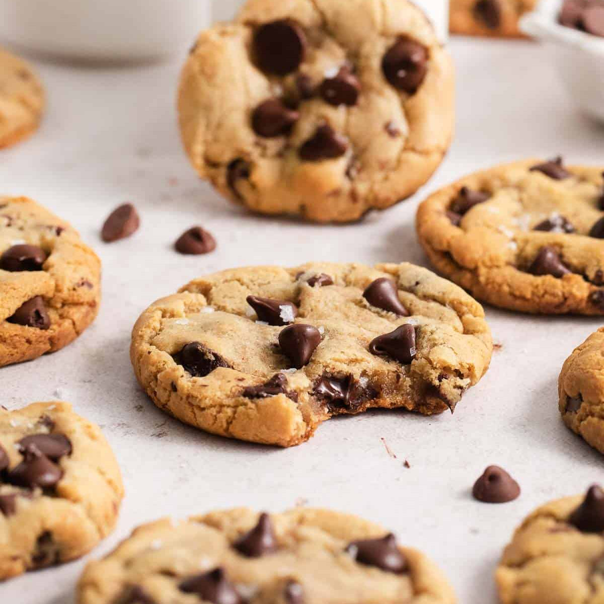 Chocolate chip cookies on a white surface with scattered chocolate chips.