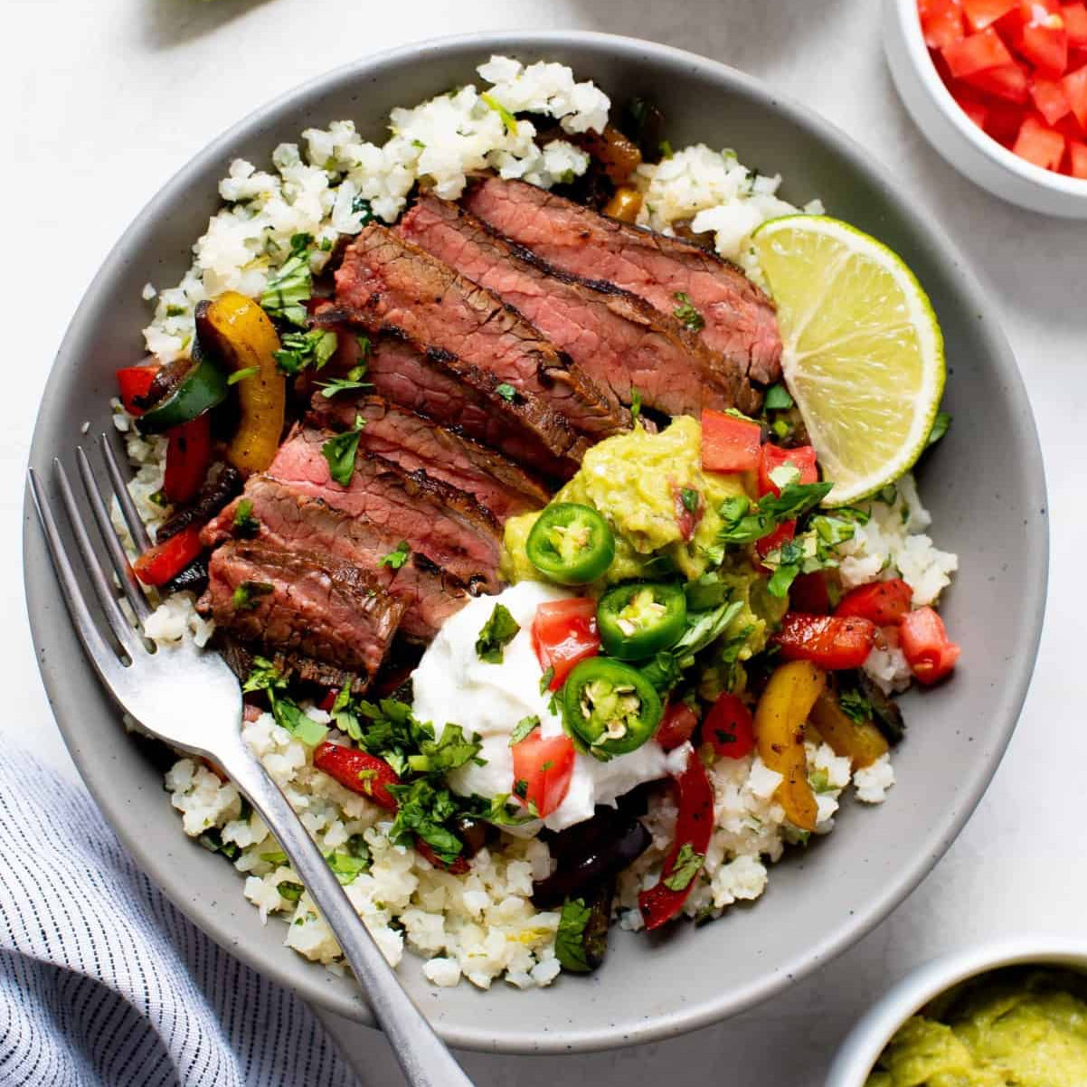 Steak bowl with cauliflower rice, vegetables, and lime on a white background
